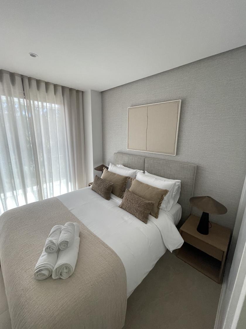 Dormitorio terminado con cama doble, cabecero gris y cortinas largas