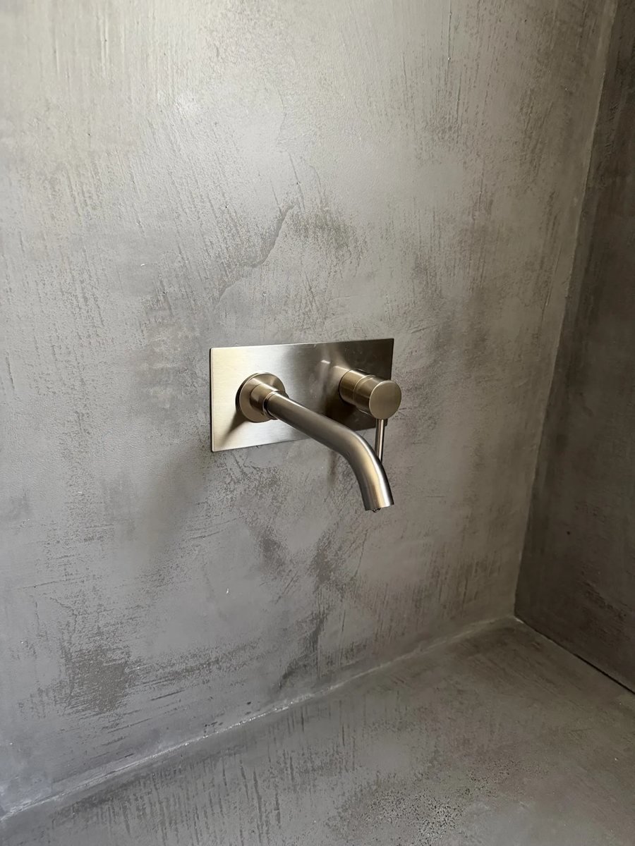 Pared de baño con microcemento gris y grifo empotrado de acero