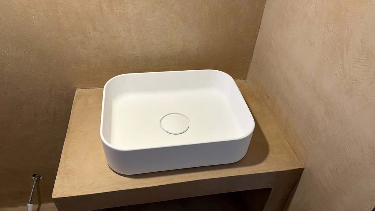 Encimera y paredes de baño con microcemento en tono arena y lavabo blanco