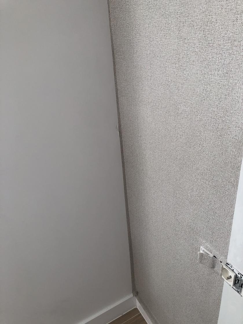 Esquina de una pared con papel pintado de efecto tejido en gris junto a una pared pintada