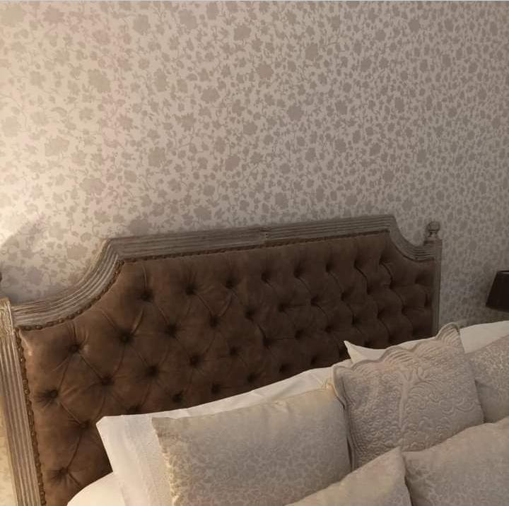 Pared de dormitorio con papel pintado floral beige tras un cabecero tapizado