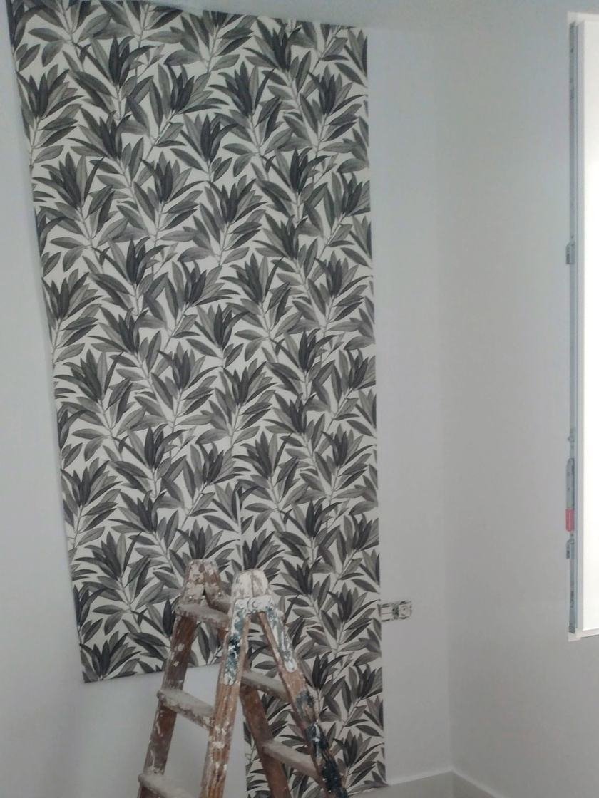 Pared de dormitorio con papel pintado de hojas en negro y gris durante la colocación