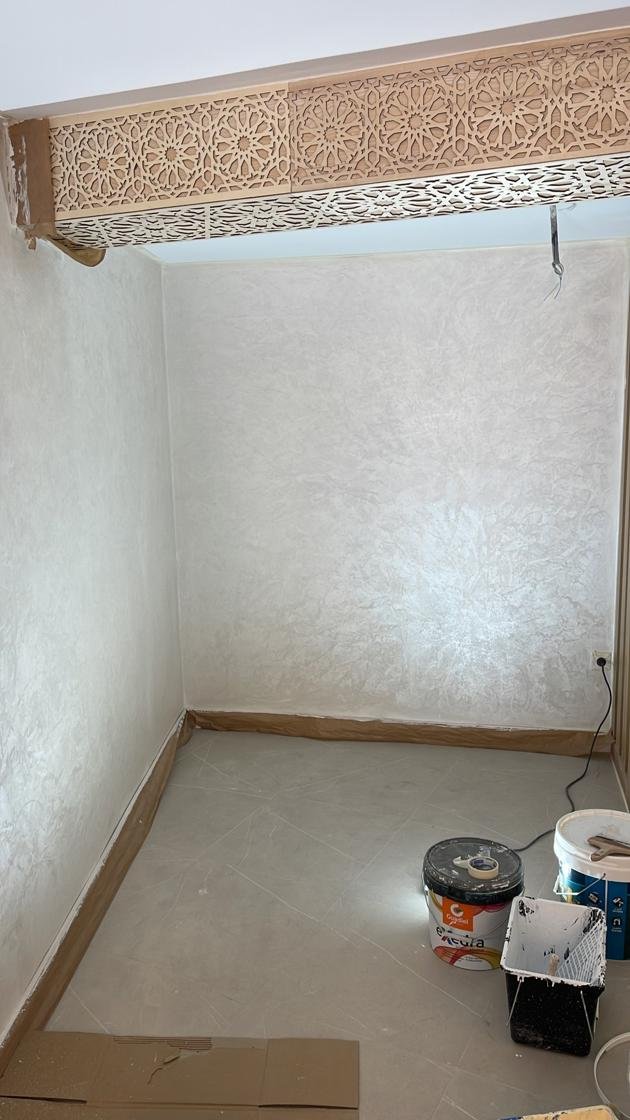 Habitación en obra con pintura decorativa efecto damasco aplicada en las paredes y friso de madera tallada