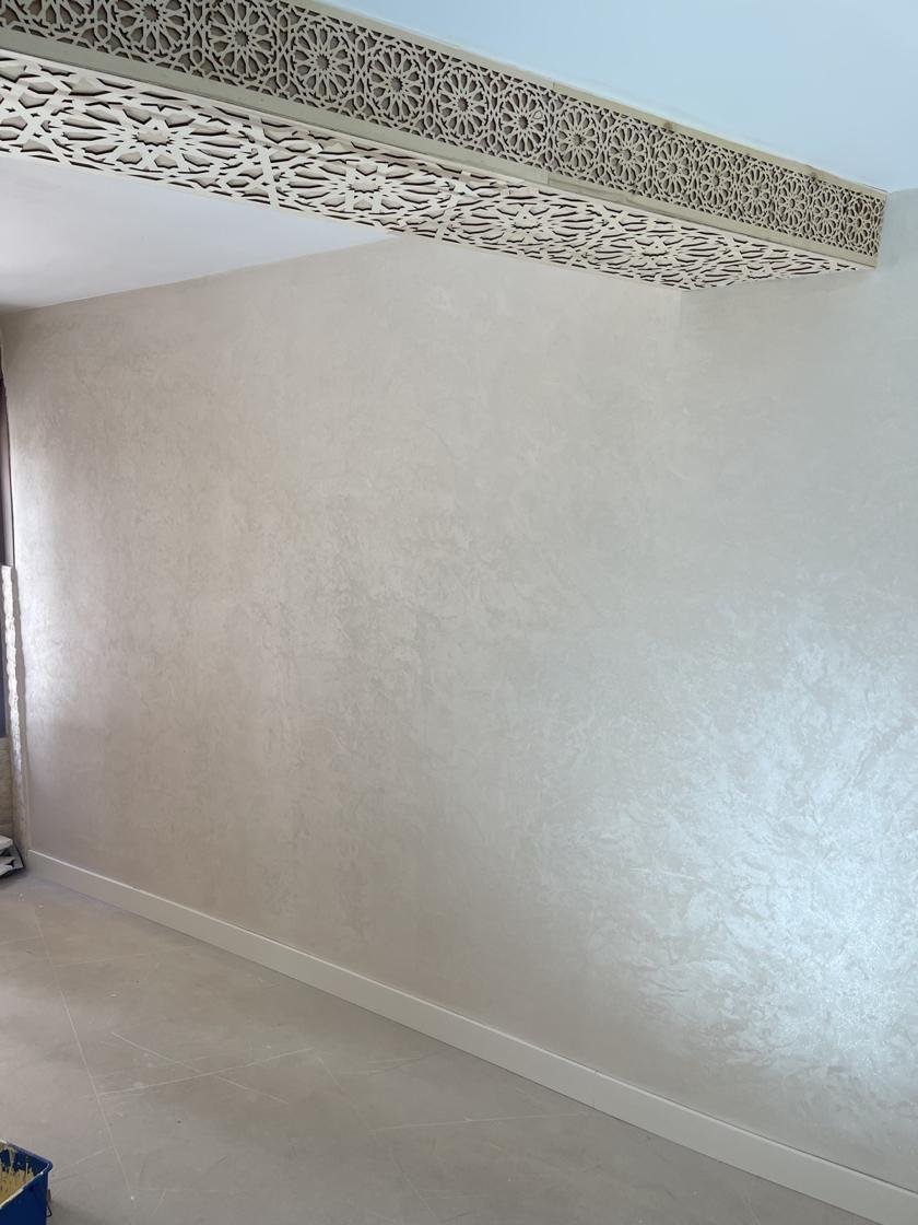 Pared con pintura decorativa efecto damasco de acabado nacarado y friso de madera tallada en el techo